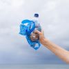 Hand holding up single-use plastic bottle and plastic bag triumphantly into the air
