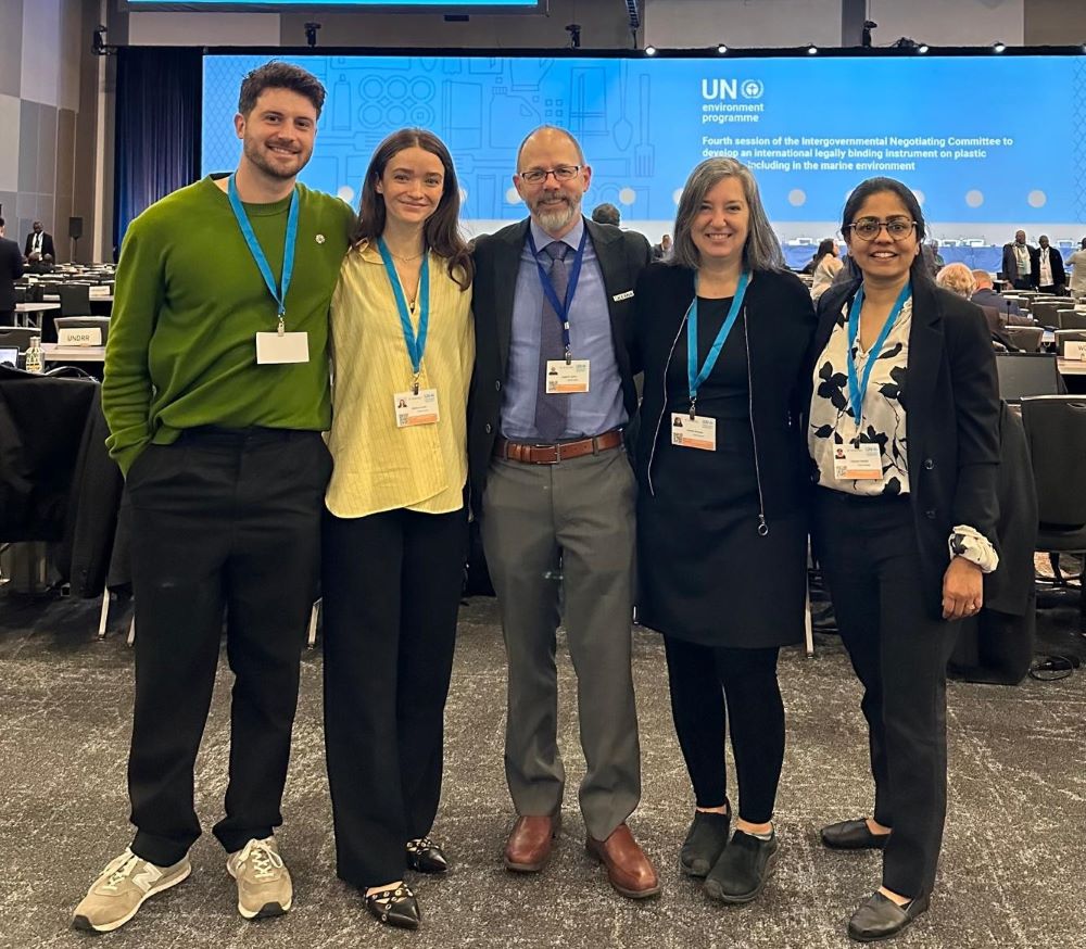 Oceana Canada staff (from left to right: Anthony Merante, Rachelle Naddaf, Josh Laughren, Kim Elmslie, Vaishali Dassani) in a conference room at INC-4 negotiations for a global plastic treaty, with blue, UN signage and rows of tables and chairs behind them.